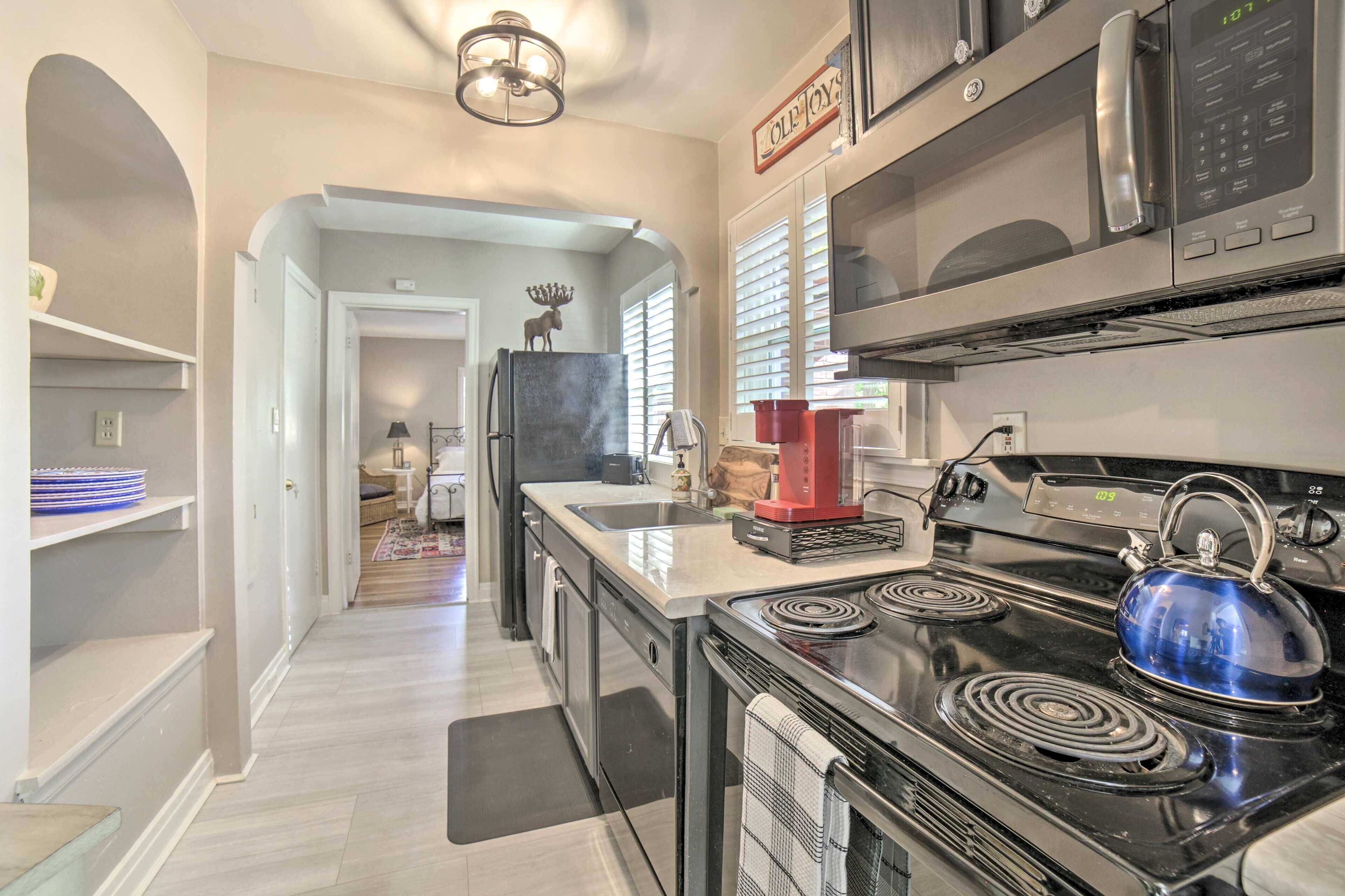 A modern kitchen with a stove, microwave, and refrigerator. There is a red coffee maker on the counter.