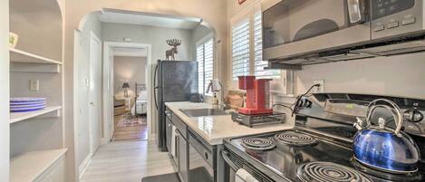 A modern kitchen with a stove, microwave, and refrigerator. There is a red coffee maker on the counter.