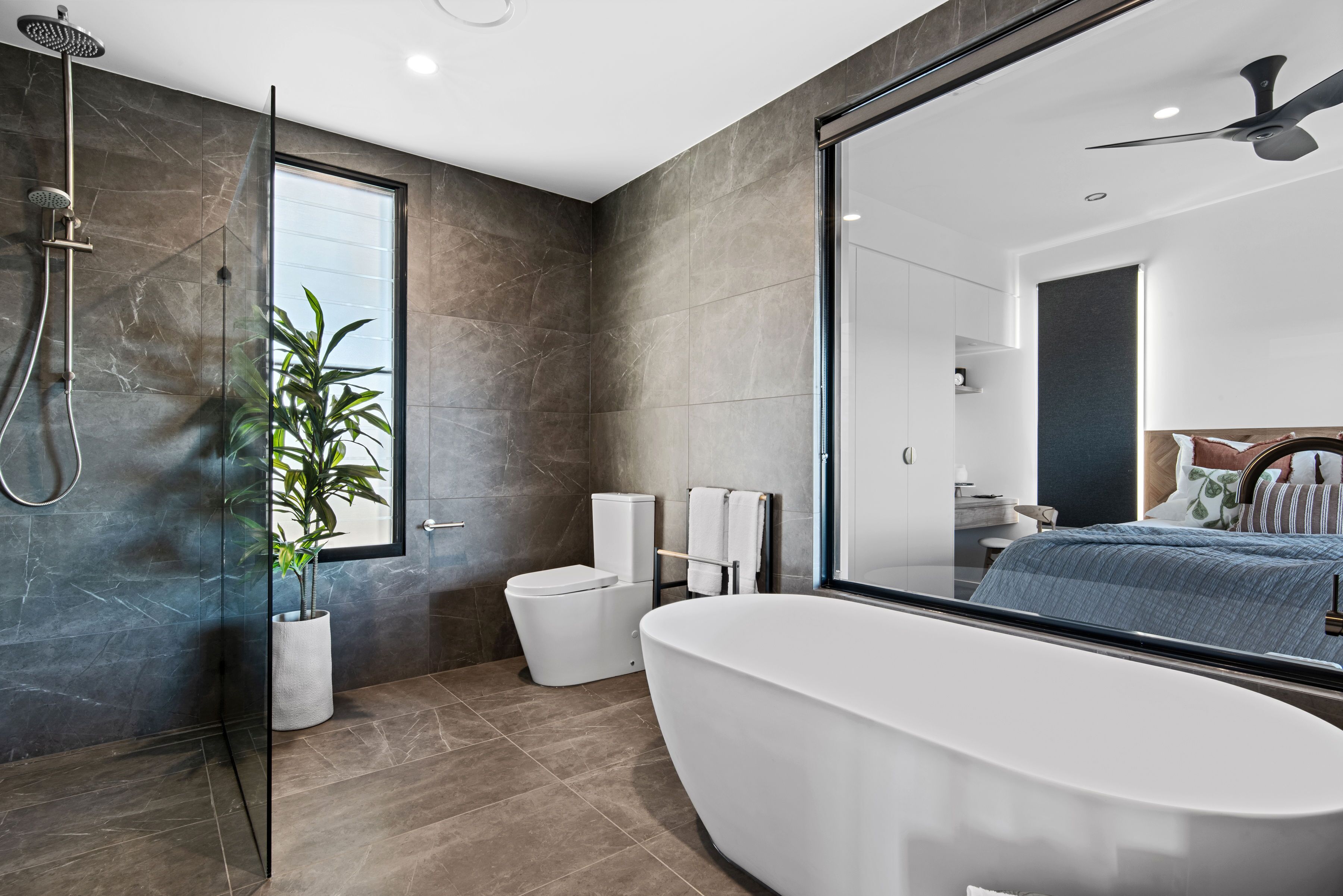 A modern bathroom with a glass-enclosed shower, a freestanding bathtub, and a potted plant.