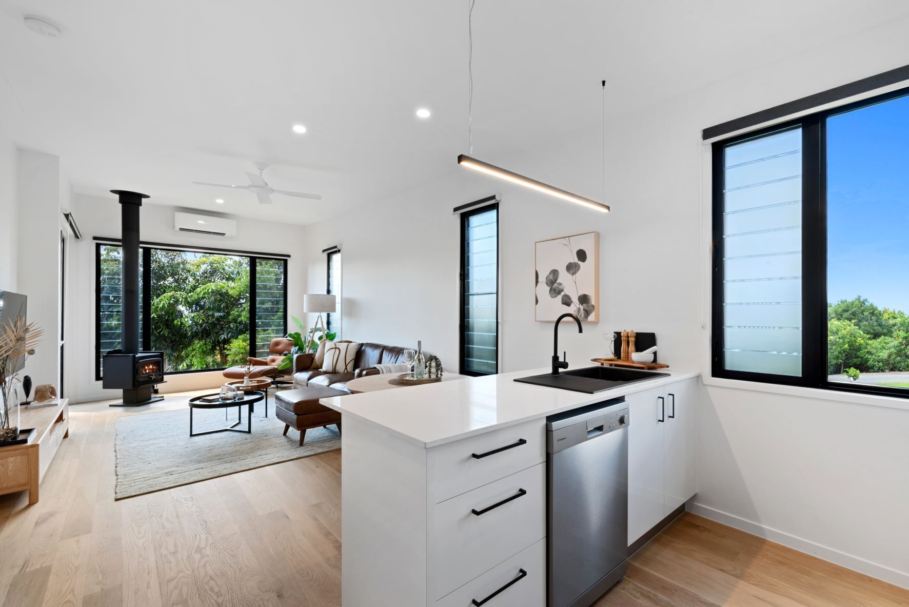 A modern kitchen with a central island, a built-in dishwasher, and a large window offering a view of greenery.