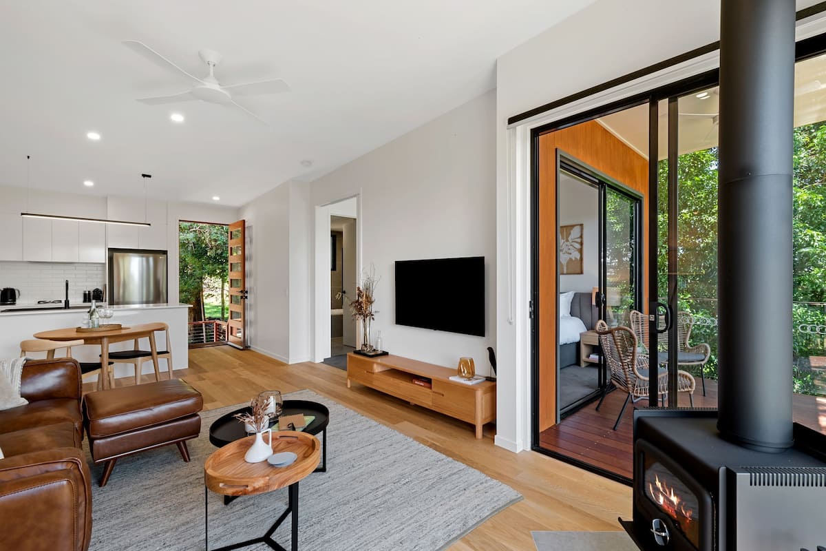 A modern living room with a fireplace, a TV, and a dining area with a kitchen in the background.