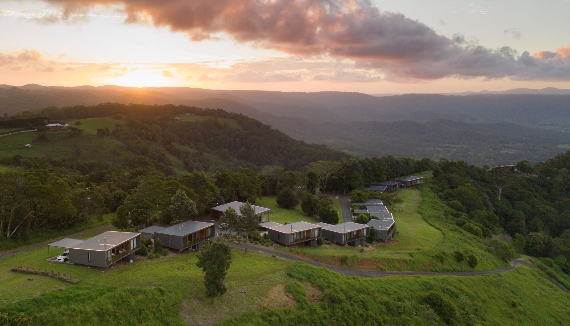 A modern residential area with multiple houses, surrounded by lush greenery and hills.