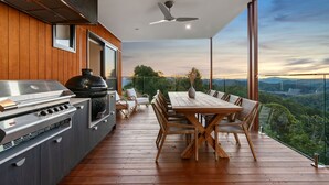 A deck with a grill, dining table, and chairs, overlooking a scenic landscape.