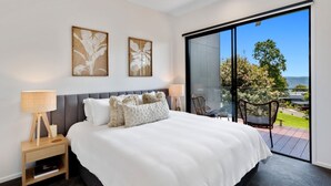 A modern bedroom with a large bed, two wall-mounted artwork pieces, a ceiling fan, and a sliding glass door leading to an outdoor patio with chairs.