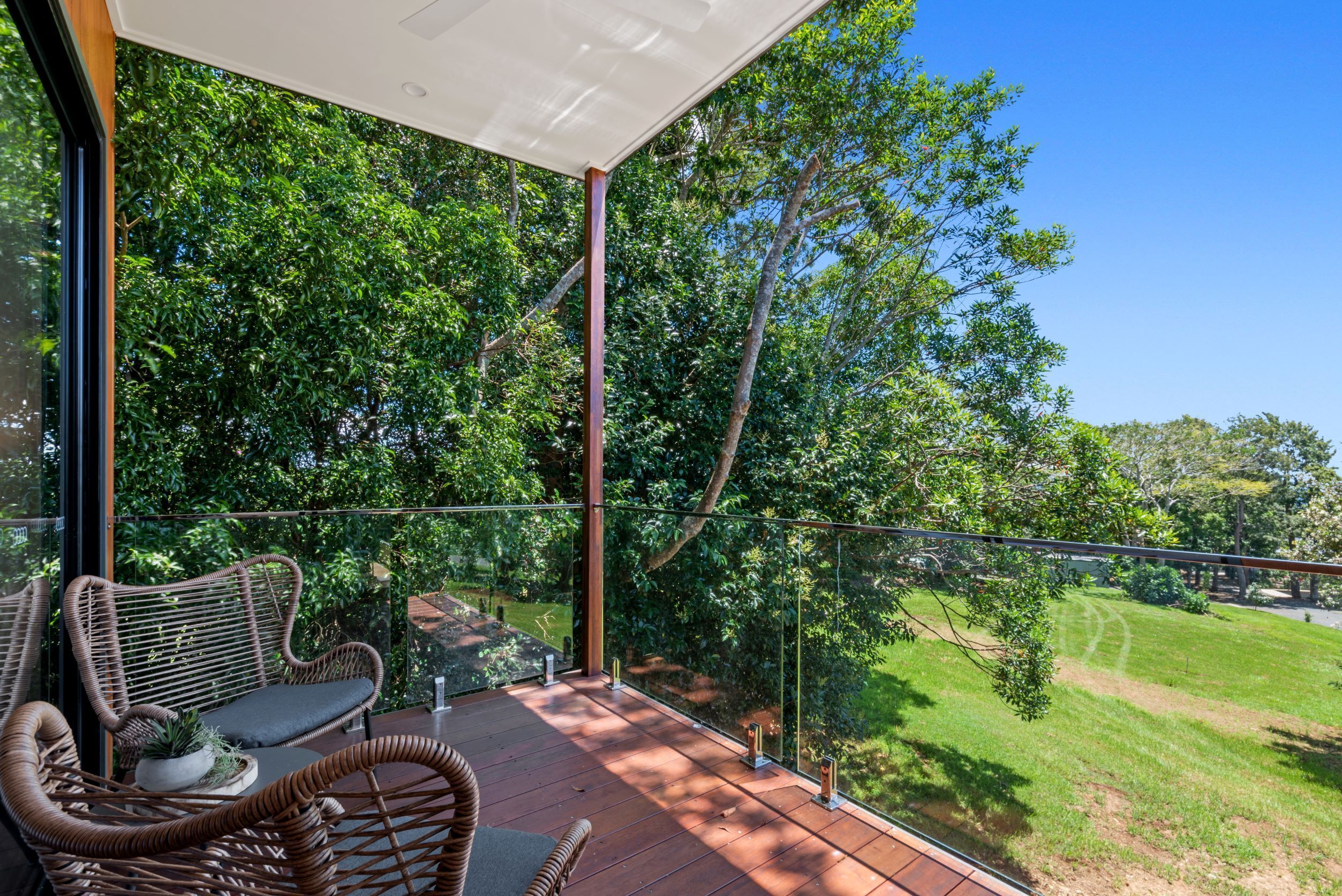 A balcony with wicker furniture, a glass railing, and a view of a green landscape.