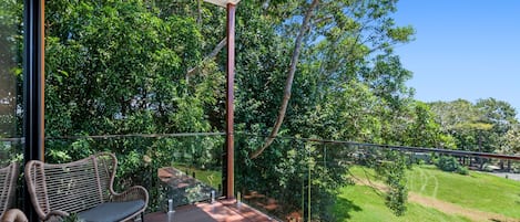 A balcony with wicker furniture, a glass railing, and a view of a green landscape.