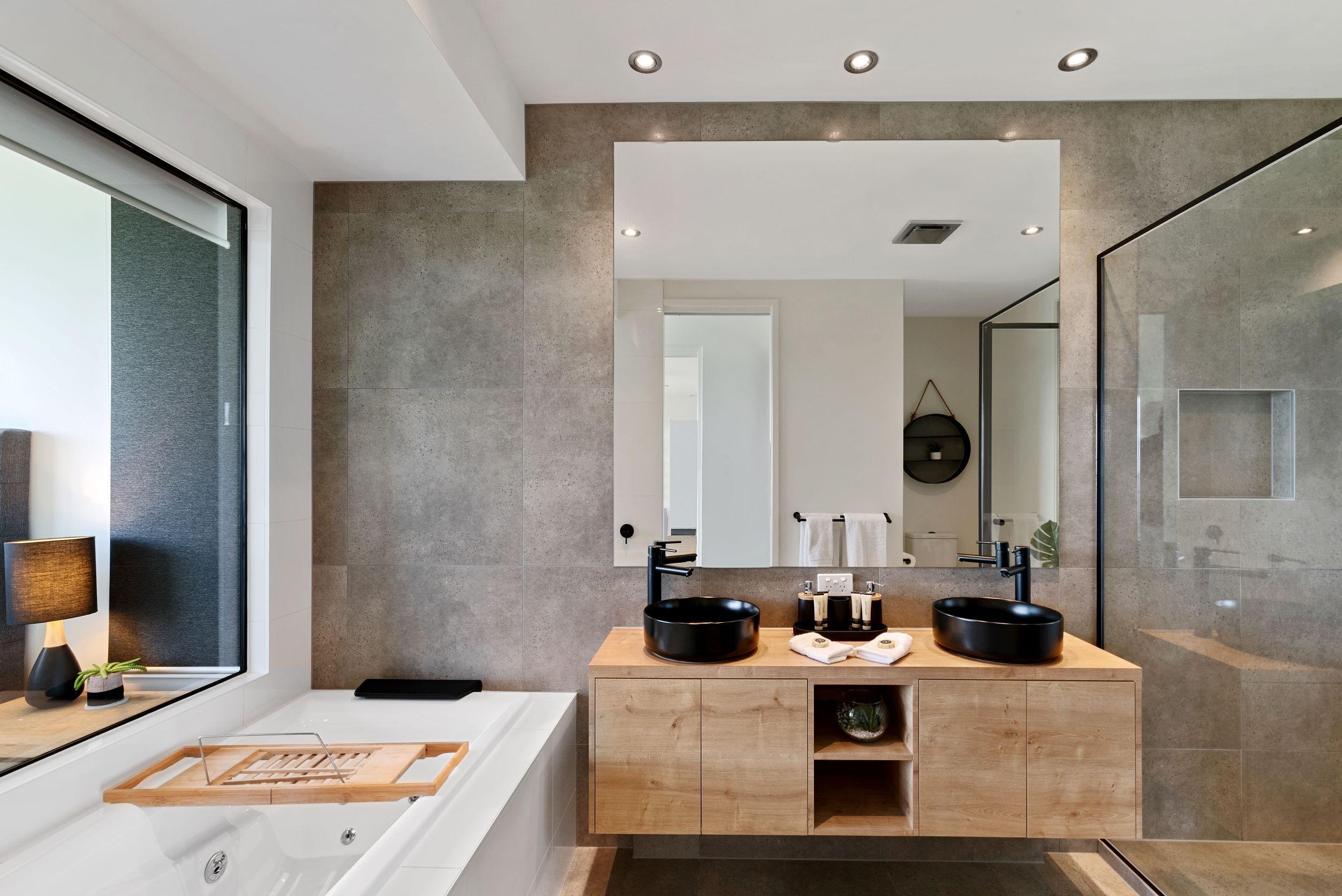 A modern bathroom with a large mirror, two black sinks, a wooden vanity, and a bathtub.
