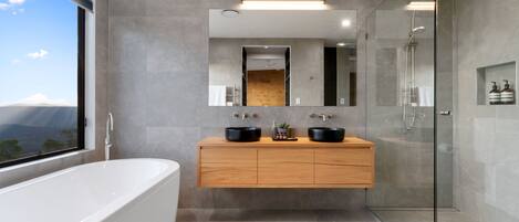 A modern bathroom with a freestanding bathtub, a wooden vanity with two black sinks, a glass shower enclosure, and a large mirror above the vanity.