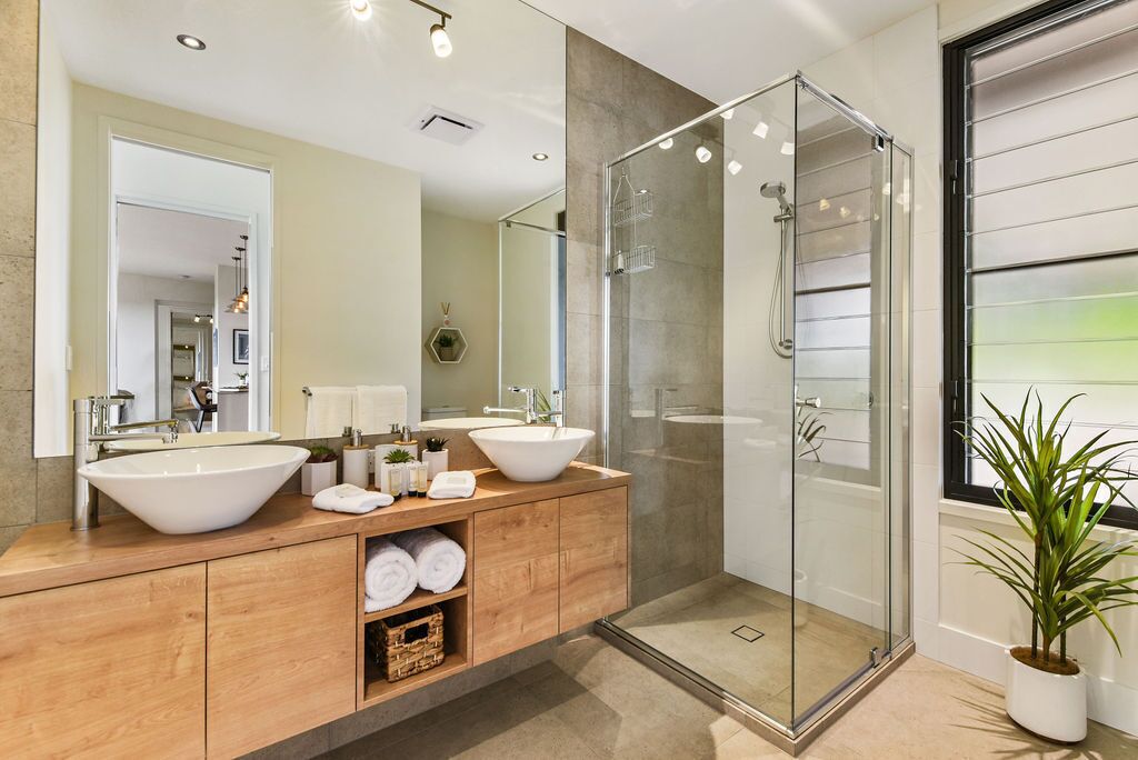 A modern bathroom with two large sinks, a glass shower enclosure, and a potted plant.