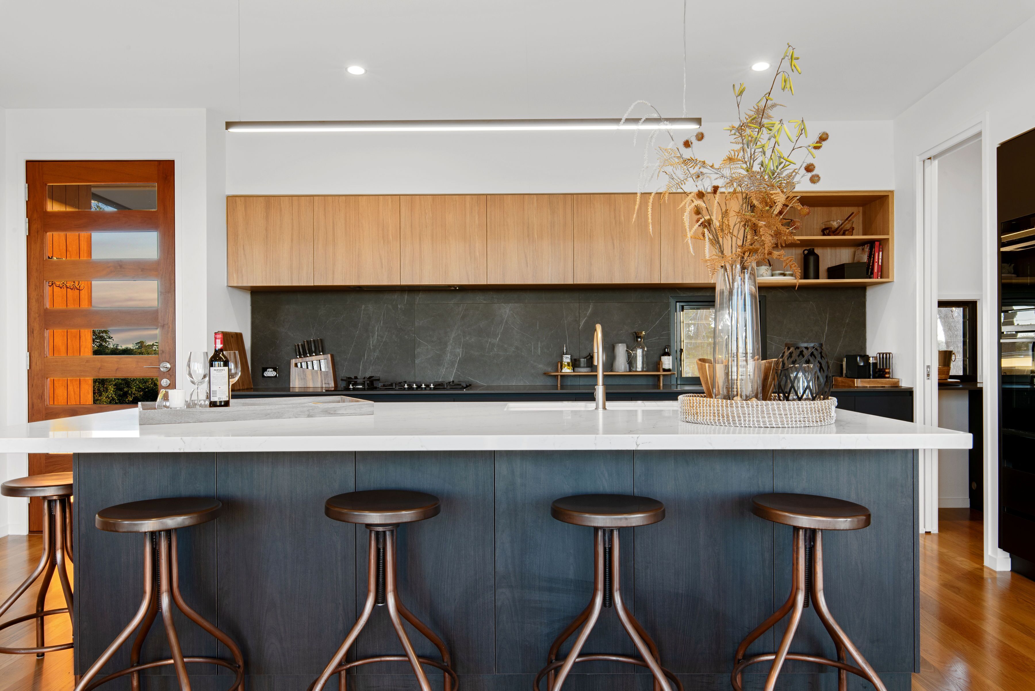 Una cocina moderna con una isla central, taburetes de bar, armarios de madera y un jarrón con plantas secas.