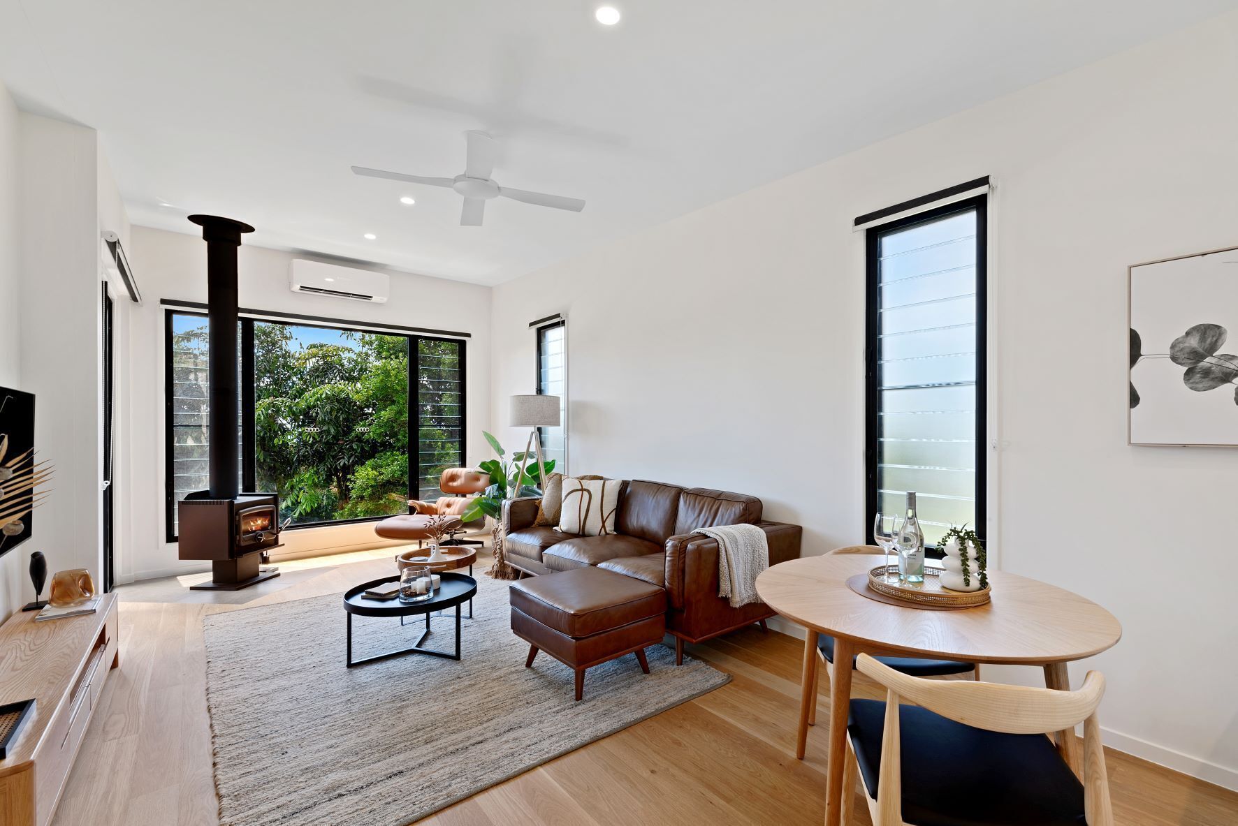 A modern living room with a fireplace, leather sofa, coffee table, and a dining area with a table and chairs.