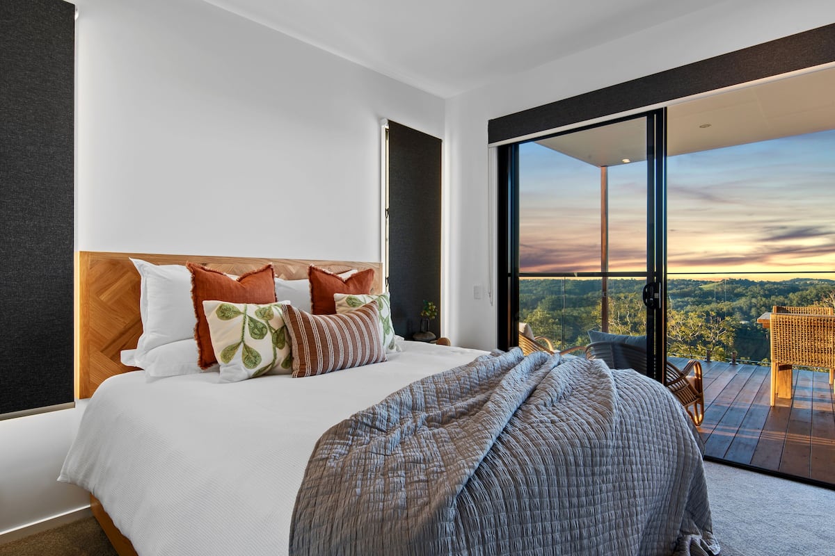 A modern bedroom with a large bed, a view of the outdoors, and a balcony with a wooden deck.
