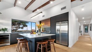A modern kitchen with a large island, bar stools, a stainless steel refrigerator, and a view of the outdoors. - The Ridge at Maleny (Booroobin)