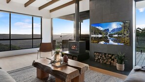 A modern living room with a large TV, a fireplace, and a scenic view through large windows. - The Ridge at Maleny (Booroobin)