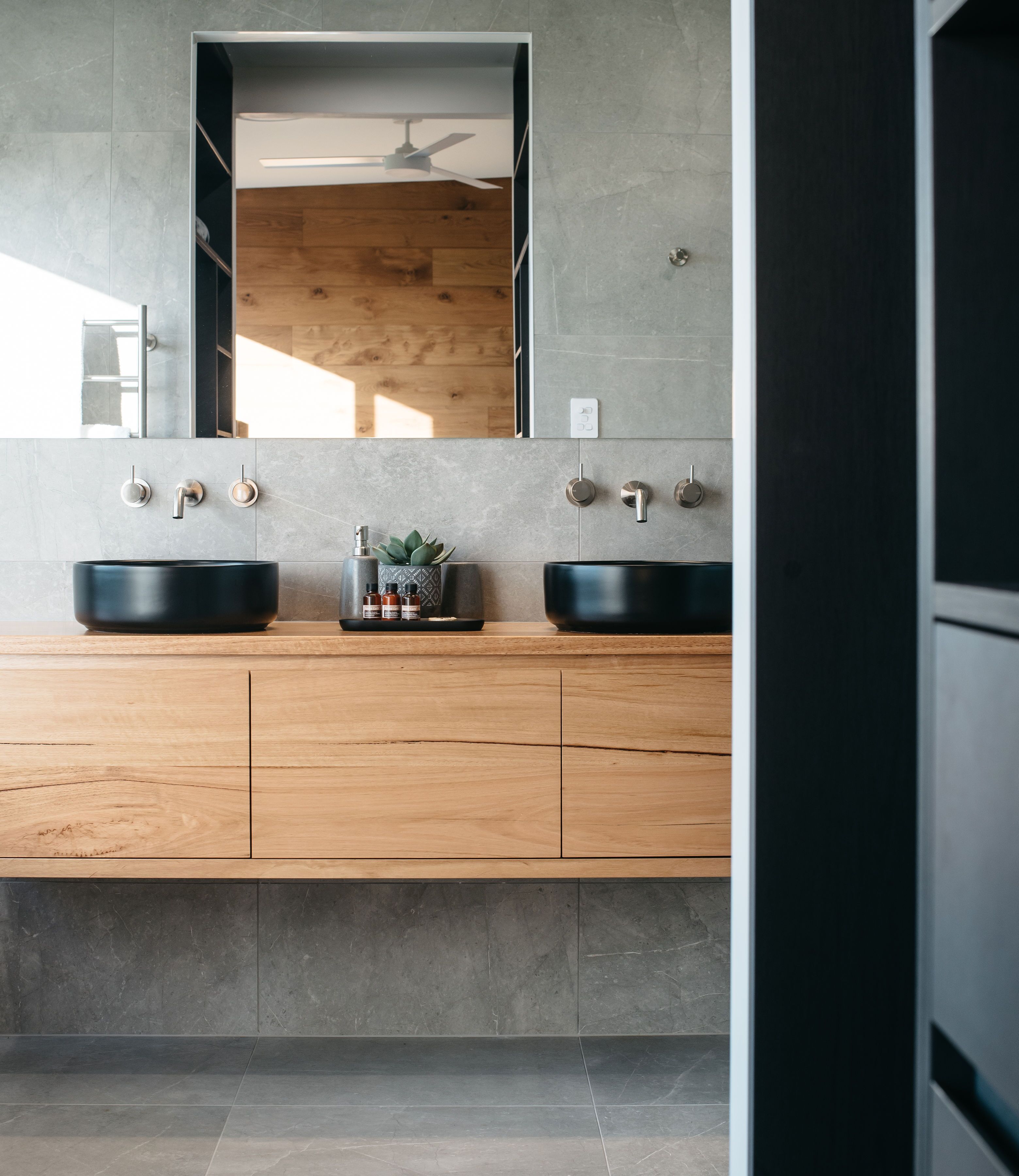A modern bathroom with two black vessel sinks, wooden cabinets, and a large mirror above.