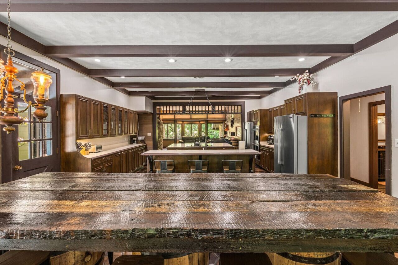 A spacious kitchen with a large wooden table, dark wooden cabinets, and a view to the outdoors.