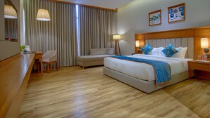 Una habitación de hotel con una cama grande, un escritorio, una silla, una lámpara y cortinas.
