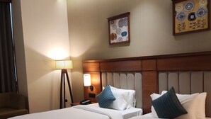 Habitación de hotel con dos camas, una mesita de noche con lámpara, una silla y obras de arte en las paredes.