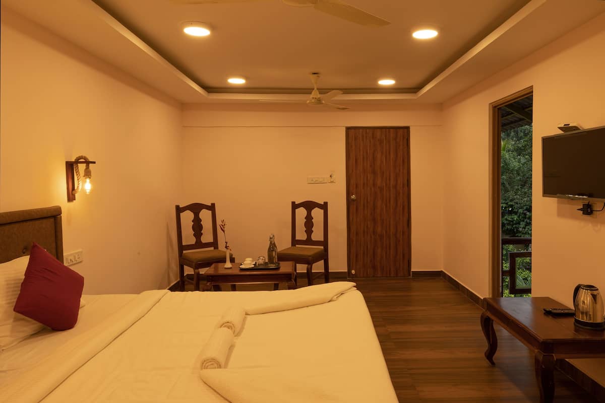 A hotel room with a bed, two chairs, a table, a TV, and a view of greenery outside.
