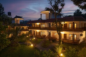 A large, multi-story building with a red-tiled roof, multiple balconies, and a well-lit exterior. - Avadale Thekkady - Stag Groups Not Allowed  (Uthamapalayam)