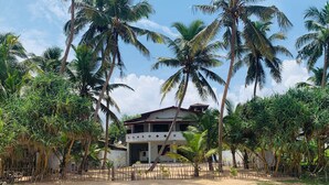A two-story house with a balcony, surrounded by palm trees and a sandy area. - Duma Beach House Front Of The Beach And Private Pool  (Ambalangoda)