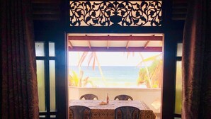 A room with a view of the ocean, a table with chairs, and a patterned curtain. - Duma Beach House Front Of The Beach And Private Pool  (Ambalangoda)