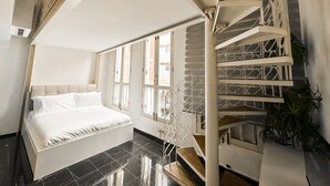 A bedroom with a bed, large windows, and a spiral staircase. - D'nova Hotel @ Bugis (Singapore)
