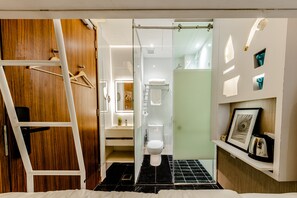 A modern bathroom with a wooden wardrobe, a white toilet, a shower area, and a shelf with a framed picture and a kettle. - D'nova Hotel @ Bugis (Singapore)