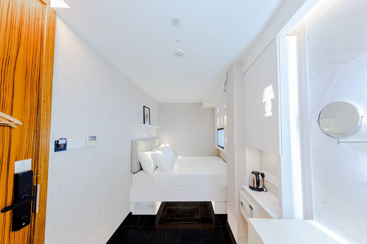A modern hotel room with a bed, bedside table, and a small seating area.
