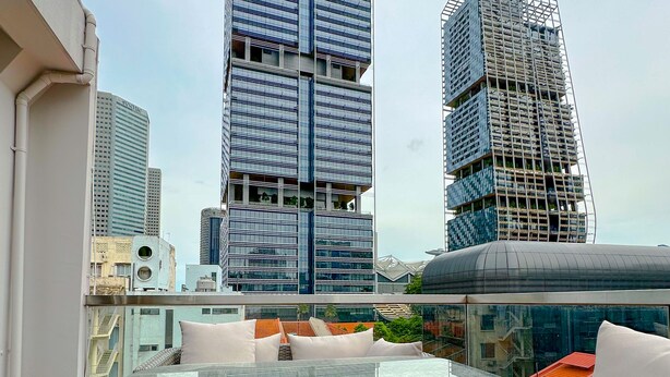 A rooftop terrace with a glass table and wicker furniture, overlooking a cityscape with modern high-rise buildings. - D'nova Hotel @ Bugis (Singapore)