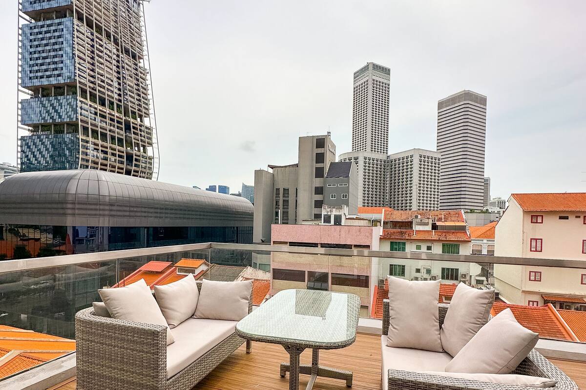 A rooftop terrace with wicker furniture, a glass table, and a view of the city skyline.