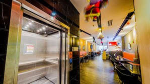A restaurant with a modern interior, including a seating area with tables and chairs, a counter, and a visible elevator. - D'nova Hotel @ Bugis (Singapore)