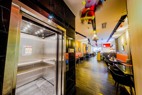 A restaurant with a modern interior, including a seating area with tables and chairs, a counter, and a visible elevator. - D'nova Hotel @ Bugis (Singapore)