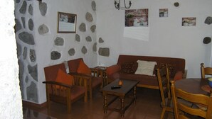 A cozy living room with a stone wall, a wooden sofa, and a dining table with chairs.