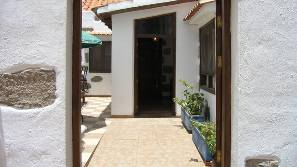 An entrance to a building with a tiled patio, a wooden door frame, and potted plants on the right.