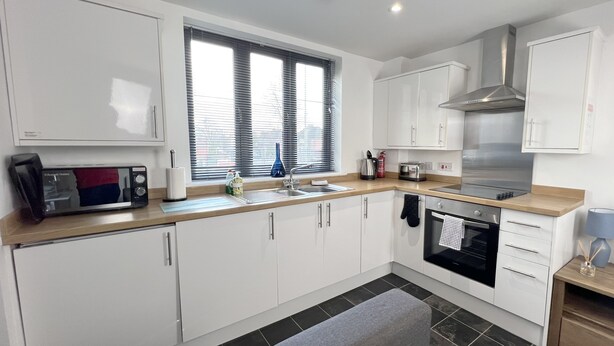 A modern kitchen with white cabinets, a built-in oven, a microwave, and a window with blinds. - 6 Cross Court, Stafford (Stafford)