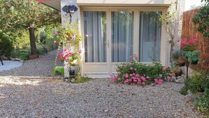 A house with a gravel driveway, a sliding glass door, and various potted plants and flowers around the entrance. - Meublé de tourisme classé 3* 35 m2 + terrasse. 2 pers, countryside VEXIN FRANçAIS (Guernes)