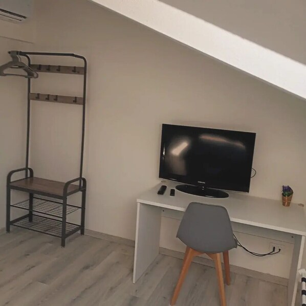 A room with a white desk, a black TV, a metal chair, and a hanging rack.