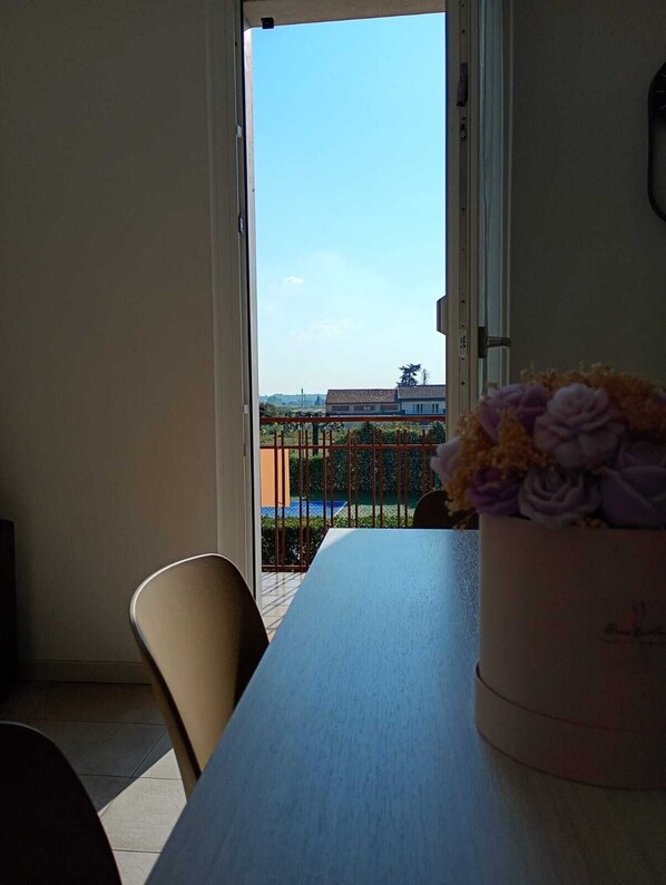 En balkon med udsigt til en swimmingpool og bygninger, et bord med en vase blomster og en stol.