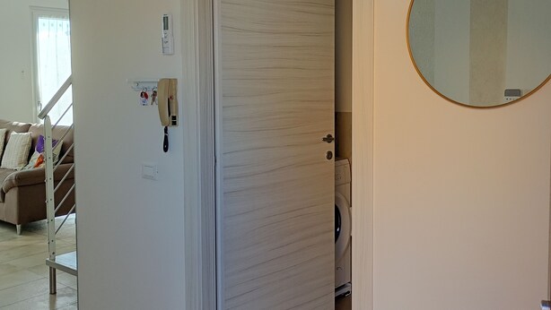 A room with a closed door, a round mirror, a thermostat, and a washing machine. - Casa Viola: Your Relaxing Retreat by the Lake (Pacengo)