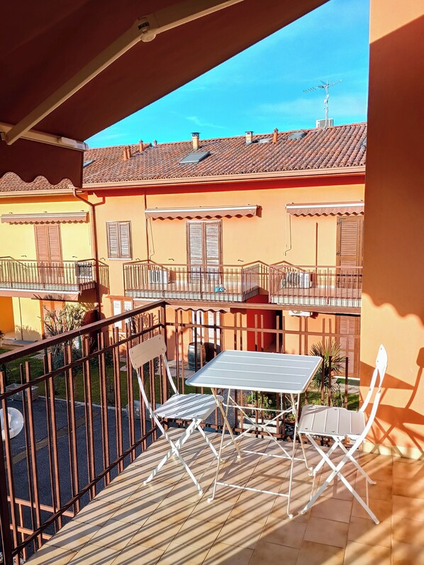 Un balcon avec une table et des chaises, une vue sur les immeubles voisins et un ciel dégagé.