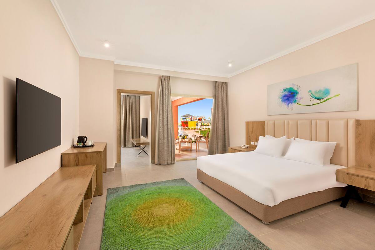 Een moderne hotelkamer met een groot bed, een flatscreen televisie, een houten bankje en uitzicht op het buitengebied.