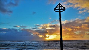 Une scène de plage avec un lampadaire au premier plan et un coucher de soleil en arrière-plan.