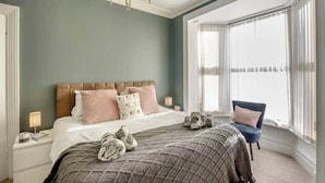 Une chambre à coucher avec un grand lit, un lustre, une fenêtre avec des rideaux légers et un fauteuil.