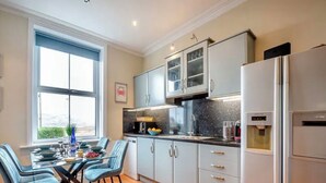 Une cuisine moderne avec des meubles de couleur claire, un réfrigérateur en acier inoxydable et un coin repas comprenant une table et des chaises en verre.