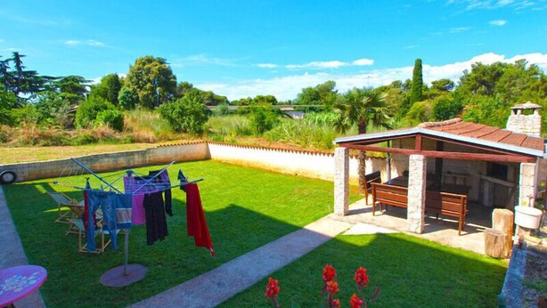 A backyard with a covered seating area, a clothesline, and a lawn.