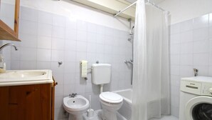 A bathroom with a sink, bidet, toilet, bathtub, and a washing machine.