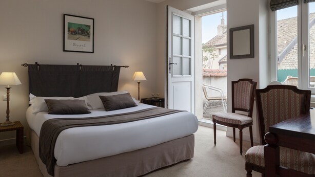 A neatly arranged bedroom with a bed, bedside lamps, a chair, and a dining table. - Hotel The Originals de la Paix Beaune (Beaune)