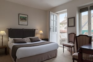 Un dormitorio ordenado con cama, lámparas de noche, una silla y una mesa de comedor.