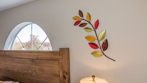 Habitación con cabecera de madera, ventana con vistas a árboles y una obra de arte con forma de hoja montada en la pared.